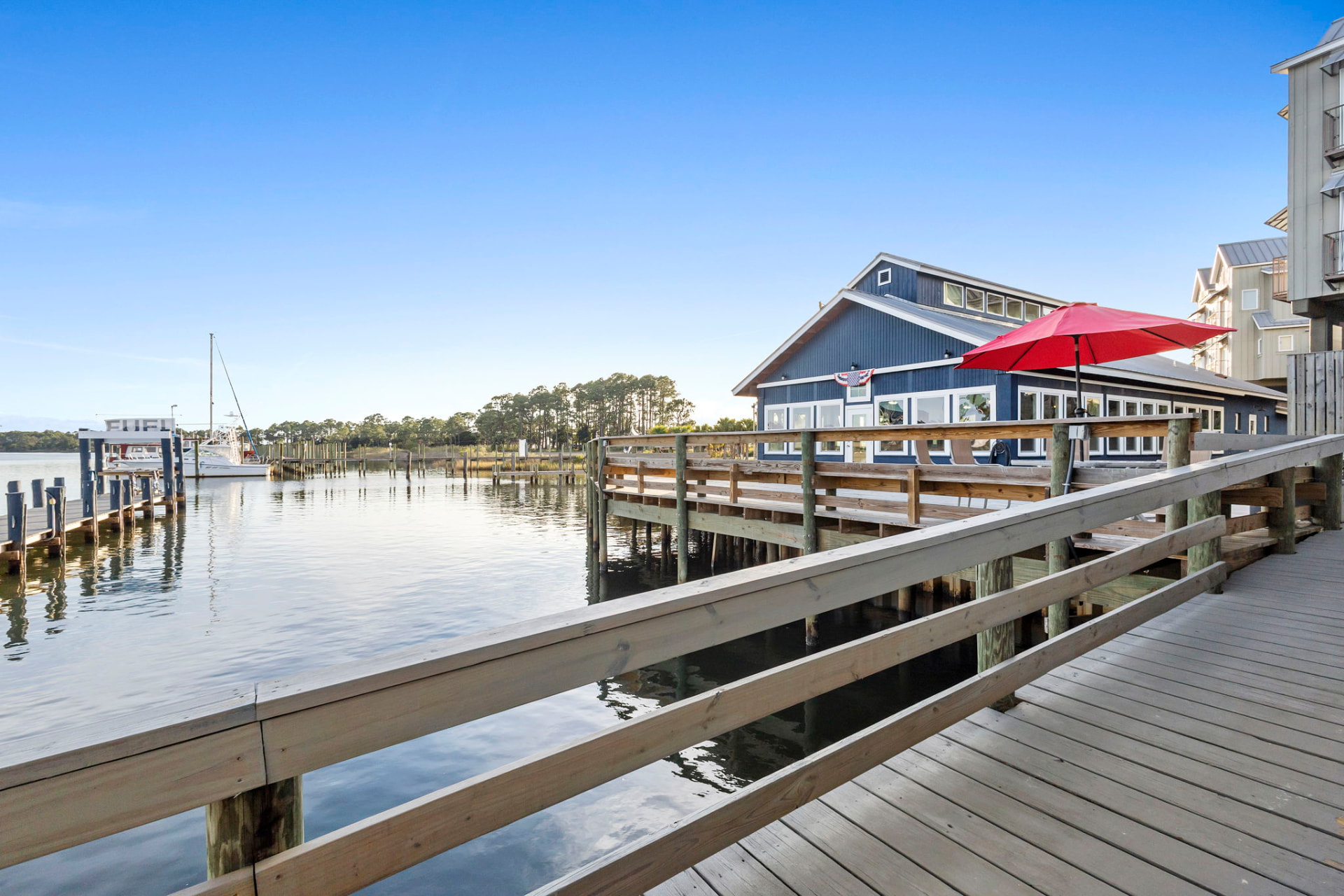 Boardwalk leading to a blue waterfront restaurant with red umbrella
